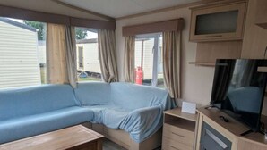 A compact RV interior with a sofa, a TV, a fireplace, and a small table.