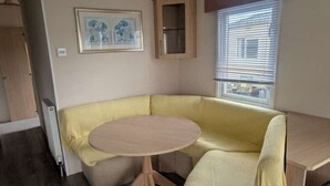A compact living space with a round table, a sofa, a cabinet, and a window with blinds.