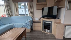 A compact living space with a sofa, a wooden table, a television, a fireplace, and a kitchen area.