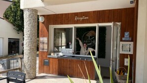 A reception area with a wooden facade, a stone pillar, and a window with a person standing inside. - Chalet with AC, pets allowed - 6 guests (Coulon)