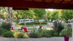 A view from a window overlooking a campsite with RVs parked, outdoor seating, and greenery. - Chalet with AC, pets allowed - 6 guests (Coulon)