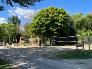 A volleyball court with a net, surrounded by trees and a playground. - Chalet with AC, pets allowed - 6 guests (Coulon)
