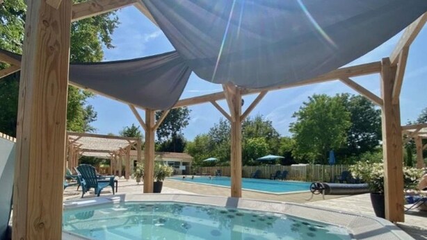 Ett bubbelbad under en träpergola med en pool i bakgrunden.