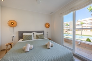 A hotel room with a bed, two wall-mounted lamps, a view of a swimming pool, and a balcony. - Casa BiBo – Comfort & Relax on the Costa Blanca (Orihuela Costa)