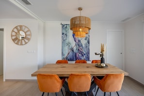 A dining area with a wooden table, orange chairs, a wall clock, and a hanging light fixture. - Casa BiBo – Comfort & Relax on the Costa Blanca (Orihuela Costa)