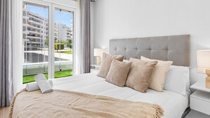 A modern hotel room with a large bed, a nightstand, a lamp, and a view of the city through floor-to-ceiling windows. - Exclusive apartment near Puerto Banús - 4 guests (Marbella)