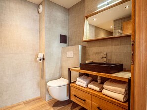 Ein modernes Badezimmer mit Toilette, einem Holzkosmetikschrank mit Waschbecken und einem Spiegel darüber.
