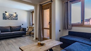 Een moderne woonkamer met een bank, een stoel, een houten tafel en een groot raam met gordijnen.