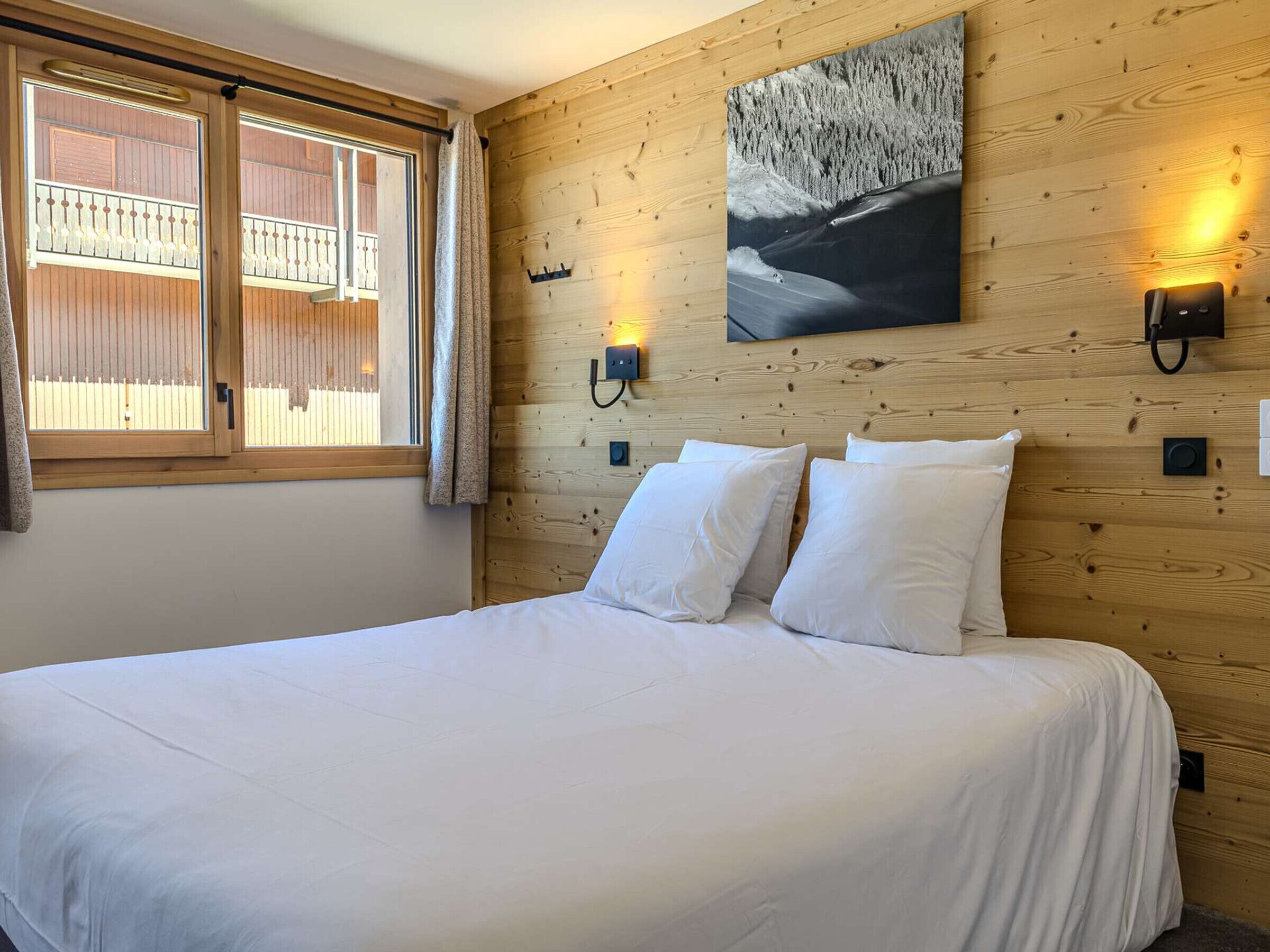 Un dormitorio con cabecera de madera, cama con ropa de cama blanca, ventana con persianas y un aplique de pared.