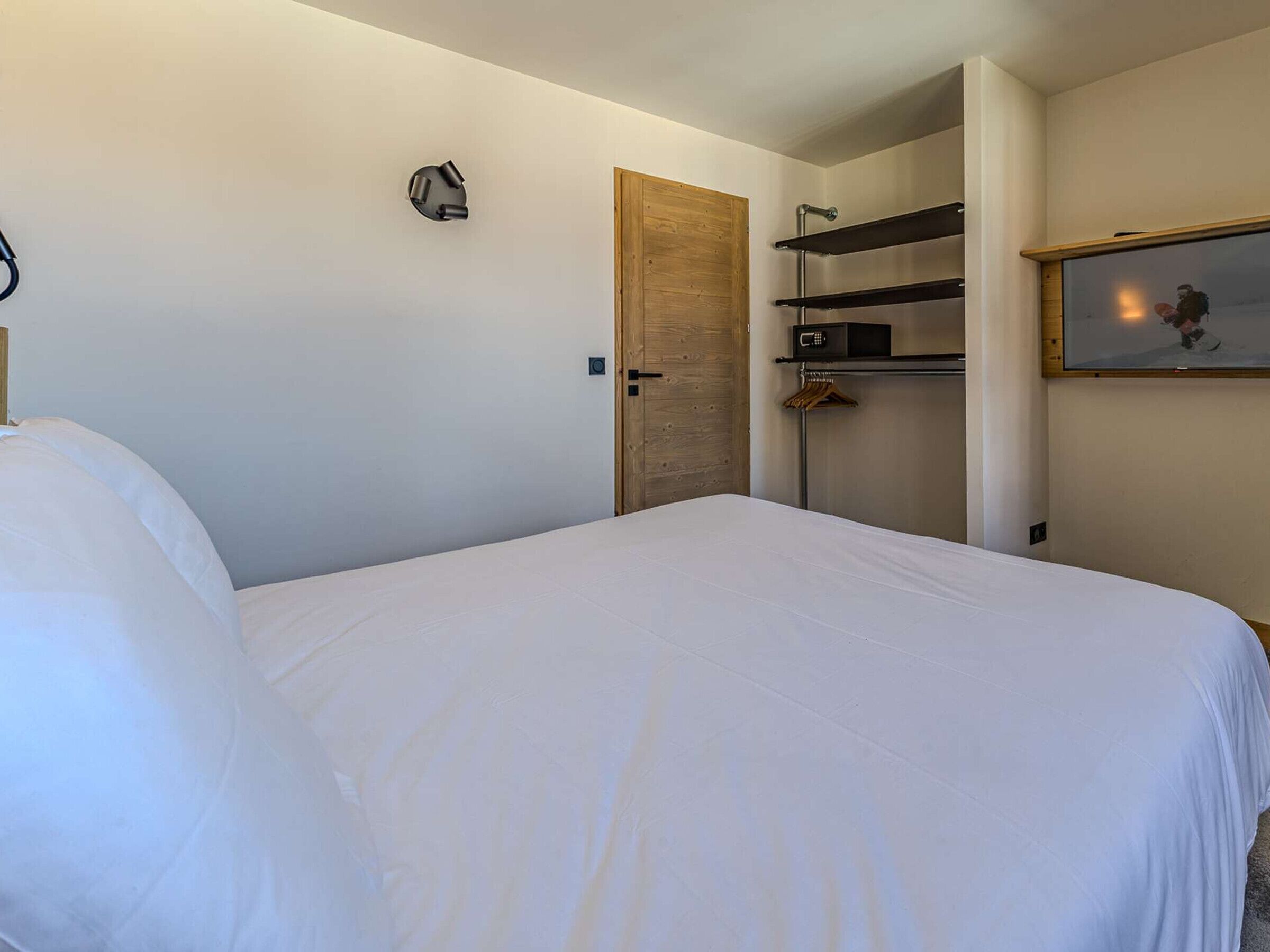 A hotel room with a bed, a wooden door, a coat rack, a wall-mounted TV, and a microwave.