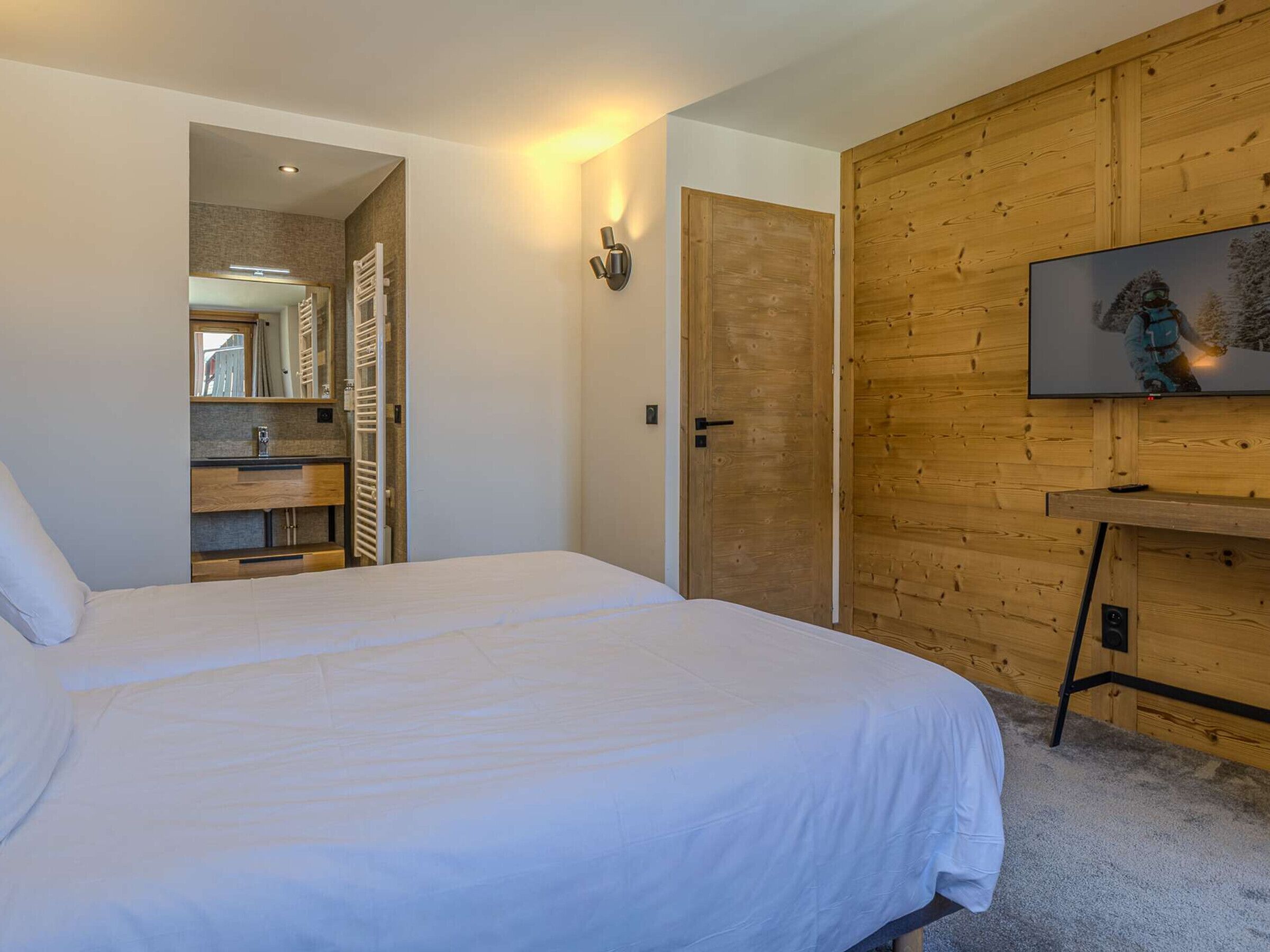 Ein Schlafzimmer mit einem Bett, einer Holzwand, einem Fernseher und einem durch eine offene Tür einsehbaren Badezimmer.