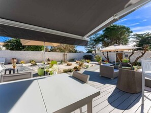 Patio esterno con tavolo e sedie, circondato da piante in vaso e un molo in legno.