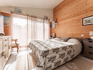 Una camera da letto con parete in legno, un letto con copripiumino decorato, una scrivania con cassetti e una sedia.