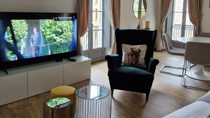 Una sala de estar con televisor, un sillón verde, una mesa de centro redonda y un sofá.