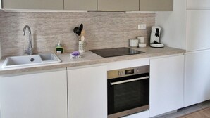 Una cocina moderna con armarios blancos, un lavamanos de acero inoxidable y un horno empotrado.
