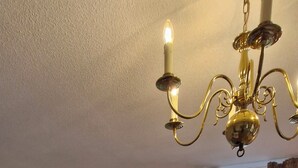 Una sala de estar con televisor de pantalla plana, un sillón negro, una araña y un ventanal con cortinas.