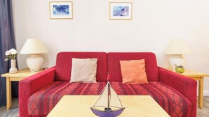 Un canapé rouge avec des coussins à motifs, une petite table sur laquelle se trouve un bol, et deux tableaux encadrés accrochés au mur.