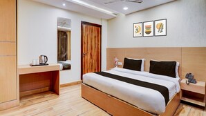 Ein Hotelzimmer mit einem hölzernen Bett, einem Schreibtisch, einem Kleiderschrank, einem Deckenventilator, eingelassener Beleuchtung und gerahmten Kunstwerken an der Wand.