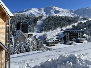 Montaña cubierta de nieve con una pista de esquí, edificios de arquitectura moderna y una estructura de madera a la izquierda.