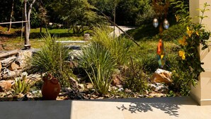 Um pátio com vista para um jardim ajardinado, um sino de vento pendurado e um vaso com planta.