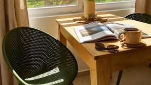 Uma mesa de madeira com uma revista, uma chávena e um vaso de flores junto a uma janela.