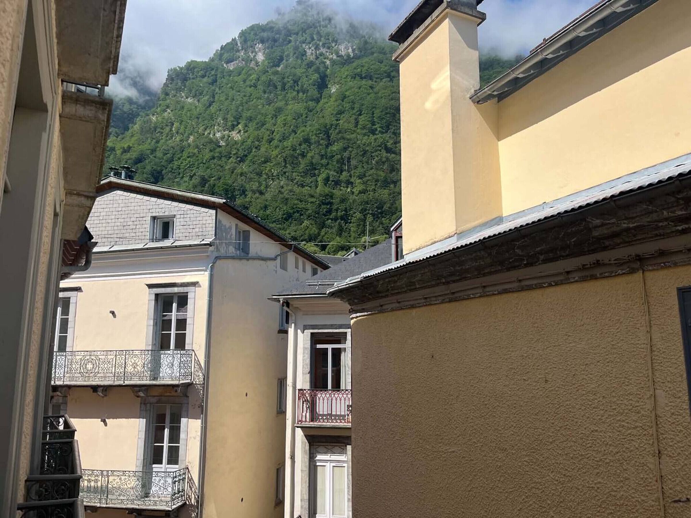 Eine enge Straße mit Gebäuden, Balkonen und einem Berg im Hintergrund.