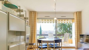 Ein modernes Wohnzimmer mit Essbereich, Fernseher und einem Balkon mit Blick auf Grünflächen.