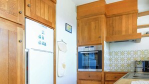 Eine Küche mit Holzausstattung, einem weißen Kühlschrank, einem Bosch-Ofen und einer gefliesten Rückwand.