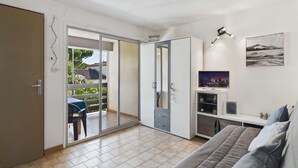 Et værelse med en skydedør til en balkon, en seng, et skrivebord med stol og et ophængt fjernsyn.