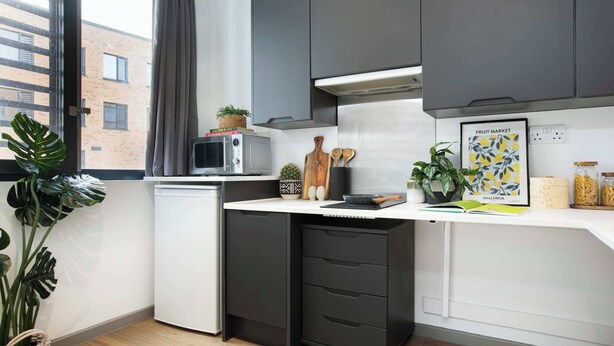 A compact kitchen with a microwave, a small refrigerator, a black cabinet, and a window with curtains.