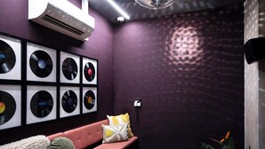 A room with a purple wall, a framed vinyl record collection, a pink sofa, a microphone, and a plant.