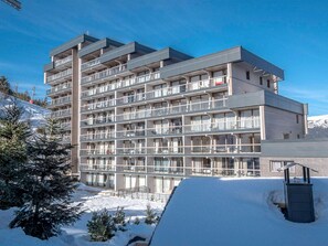 Ett hotell med flera våningar och balkonger, en skidbacke i bakgrunden och snö på marken.