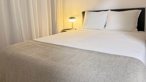 Ein ordentlich bezogenes Bett mit weißen Leinen, einer Nachttischlampe und einem Kopfteil.