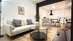Ein modernes Wohnzimmer mit Sofa, Sessel, Glastisch und Fernsehschrank.
