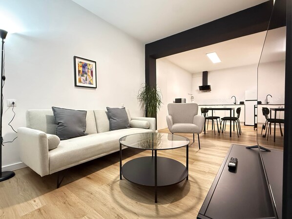 Un salon moderne comprenant un canapé, un fauteuil, une table basse en verre et un meuble pour la télévision.