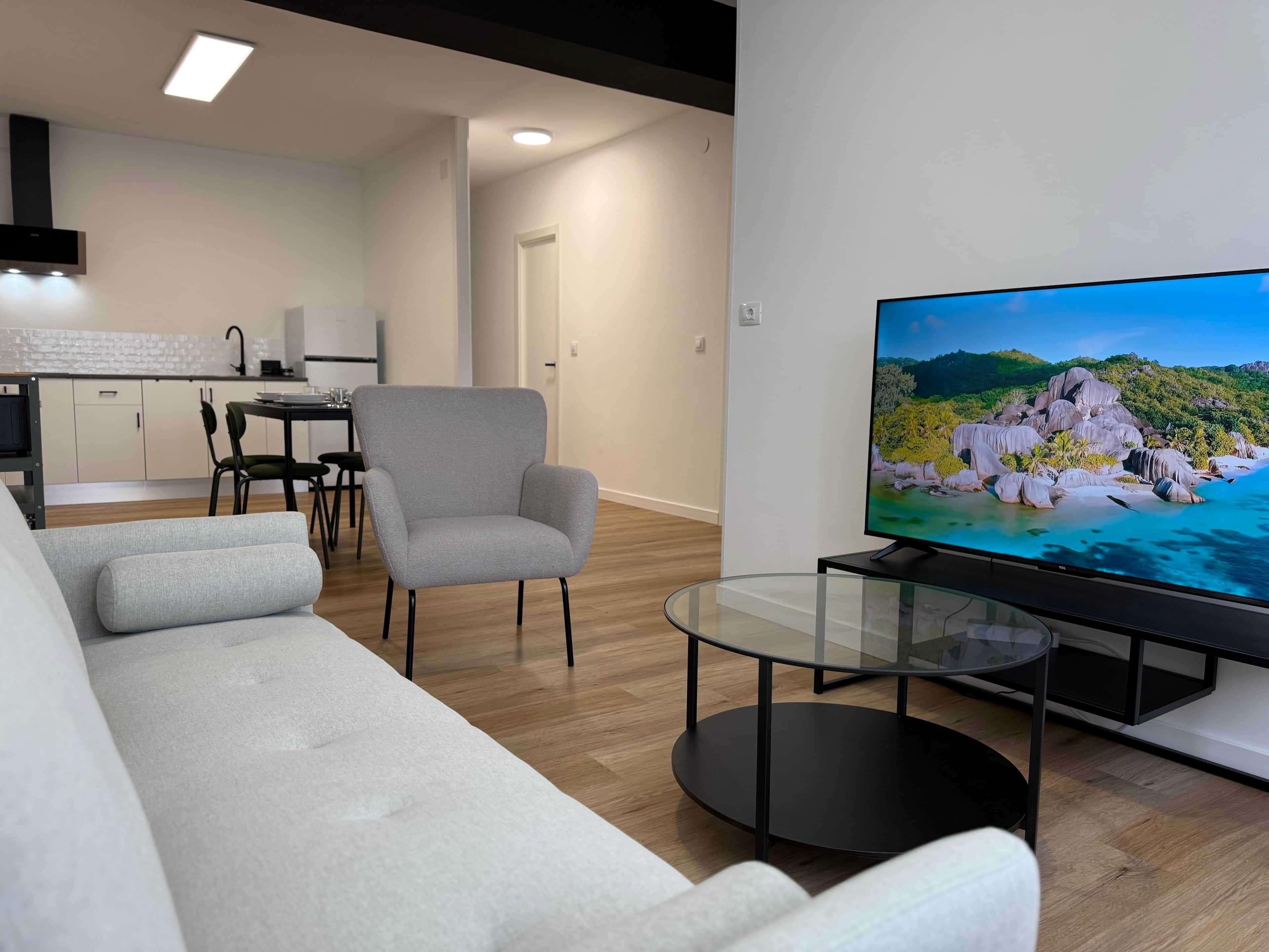 Een moderne woonkamer met een bank, fauteuil en een televisie op een glazen salontafel.