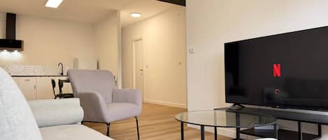 Una sala moderna con un sofá, un sillón, una mesa de centro de vidrio y un televisor de pantalla plana mostrando el logotipo de Netflix.