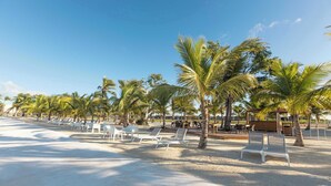 A beach with white lounge chairs and palm trees. - NOK Stylish 1BR Apartment With Rooftop Terrace BBQ By Vistacana Rentals (Punta Cana)