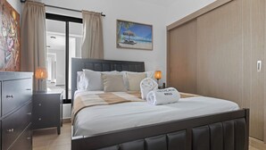 A hotel room with a bed, nightstands, a painting, a wardrobe, and a view of the beach. - NOK Stylish 1BR Apartment With Rooftop Terrace BBQ By Vistacana Rentals (Punta Cana)