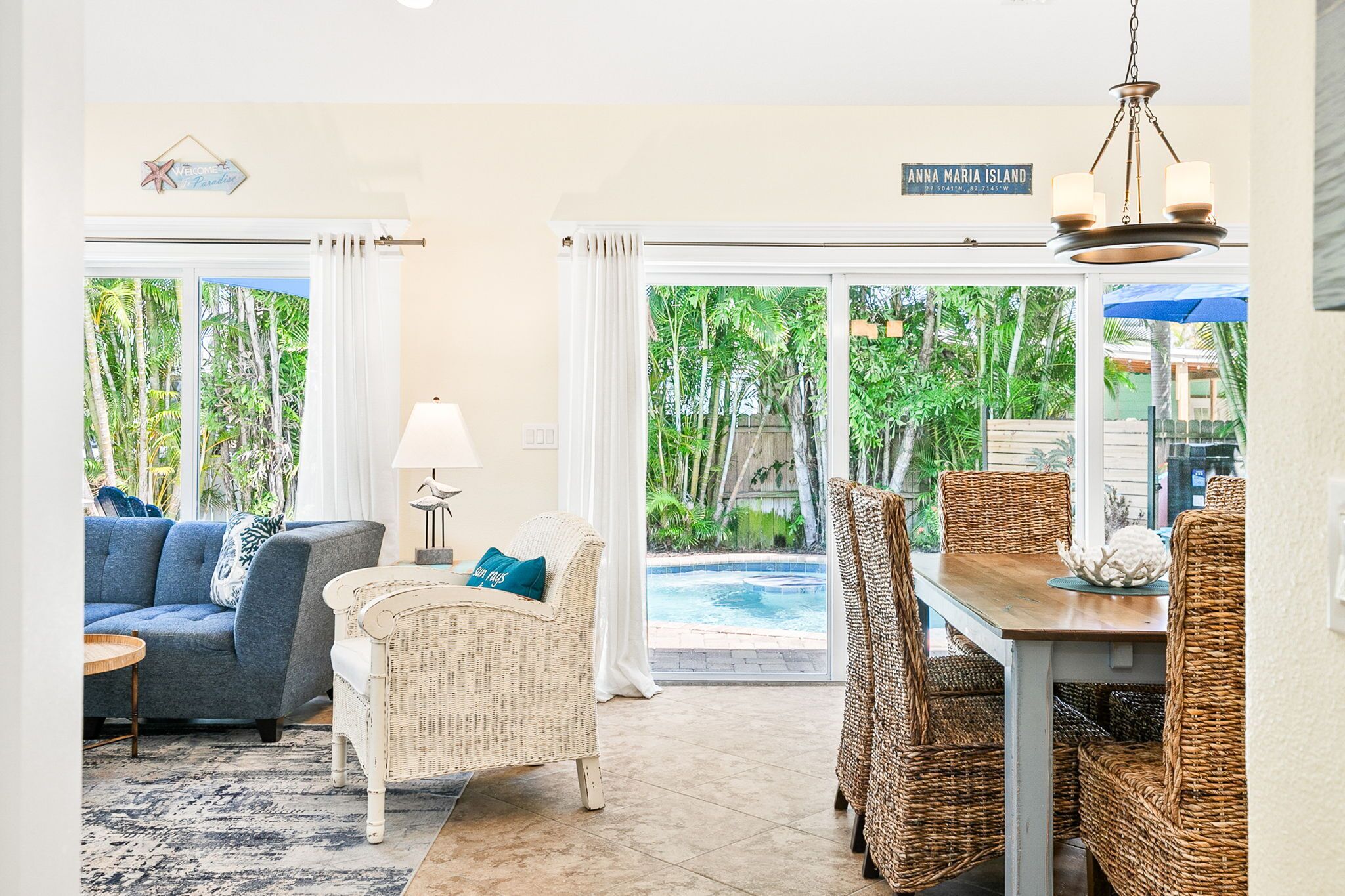 A living room with a sofa, wicker chairs, a dining table, and a view of a swimming pool.