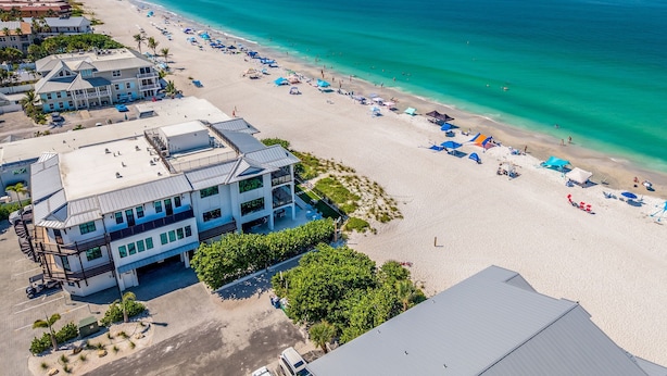 Een hotel aan het strand met meerdere balkons, een zandstrand en helder turquoise water.
