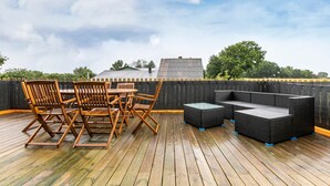 A wooden deck with a table and chairs, a wicker sofa, and a view of the sky and trees.