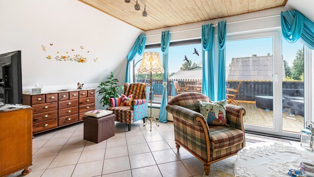 A spacious living room with a wooden ceiling, a large window with curtains, a television, a wooden cabinet, and a plaid sofa.
