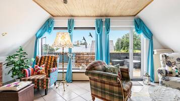 Une pièce chaleureuse avec un plafond en bois, une grande fenêtre avec des rideaux, un canapé, un fauteuil, une table et une lampe.