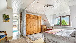 A bedroom with a bed, a wooden wardrobe, a desk, and a window with a view.