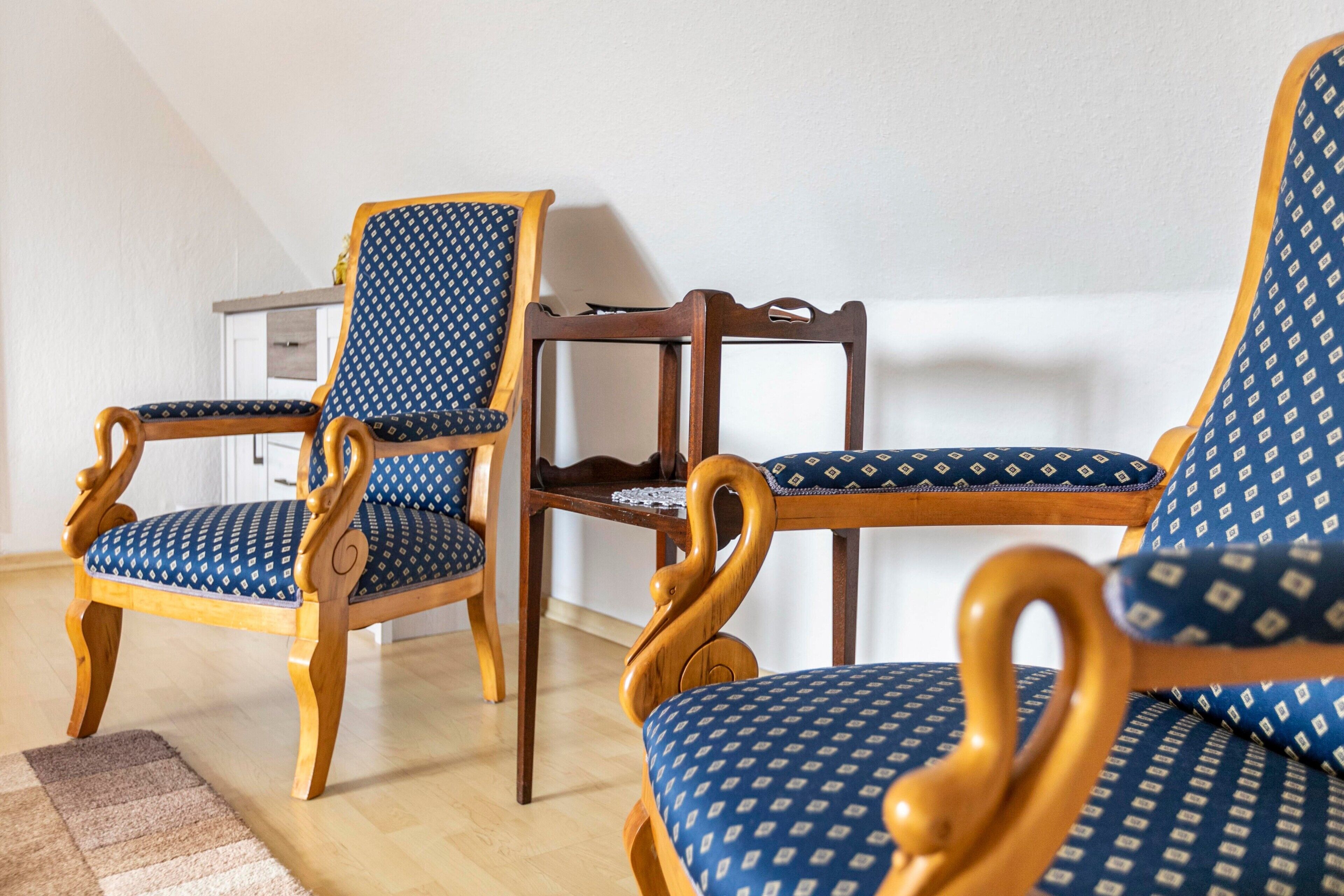 Una habitación con dos sillas de madera con tapicería azul estampada y una mesa de madera.