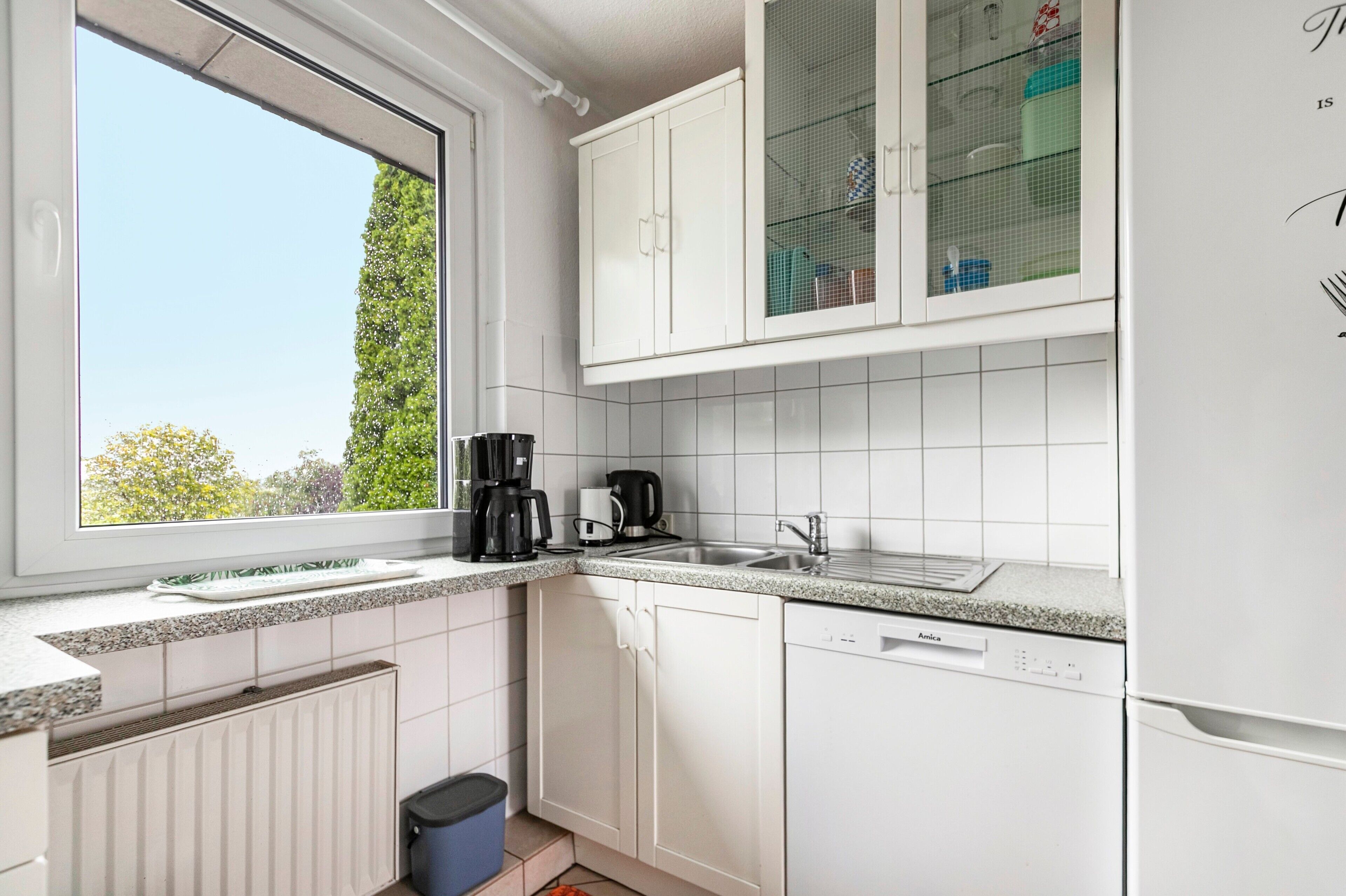 Eine Küche mit weißen Schränken, einem Fenster, einer Kaffeemaschine und einem Geschirrspüler.