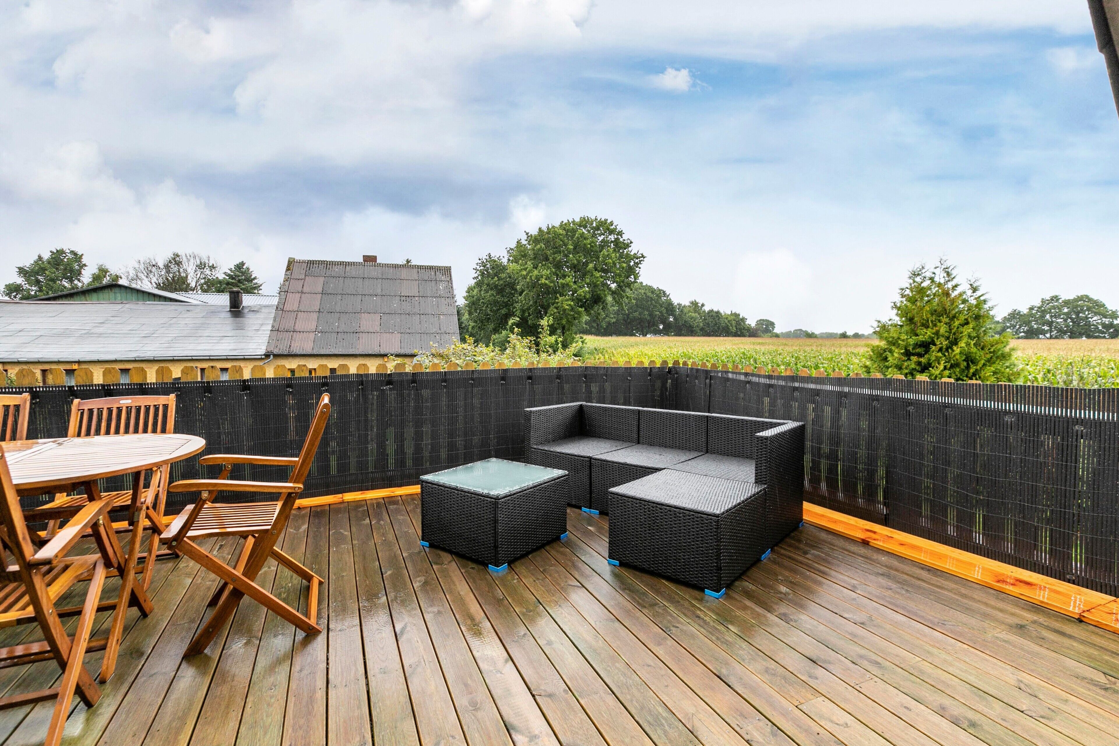 A wooden deck with outdoor furniture, including a table and chairs, and a black outdoor sofa.