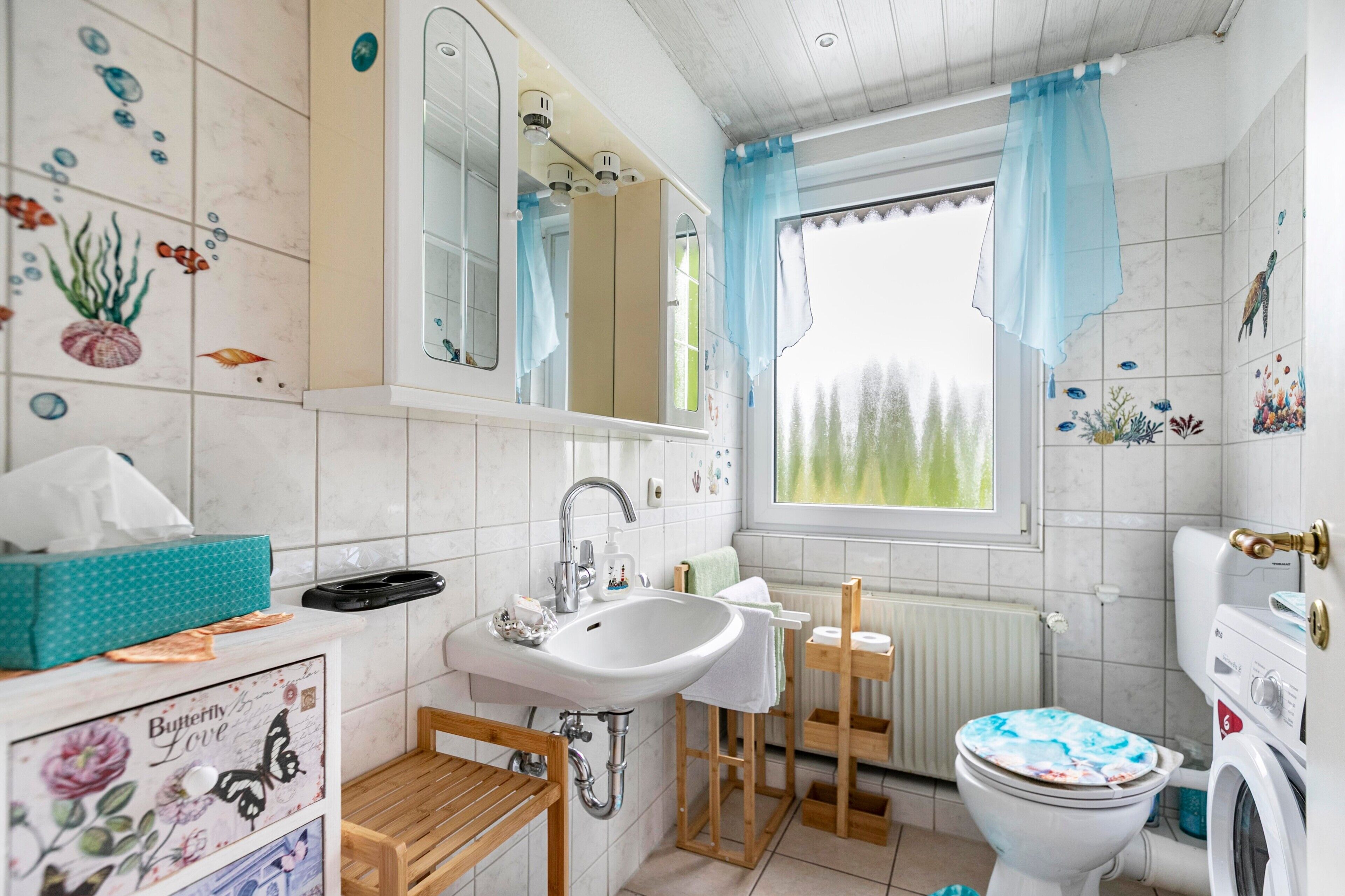 Ein Badezimmer mit Waschbecken, Spiegel, Toilette und einem Fenster mit Vorhängen.