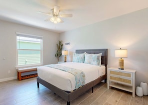 Une chambre à coucher comprenant un lit, une table de chevet, un banc, un ventilateur de plafond, une fenêtre et un panneau décoratif mural.
